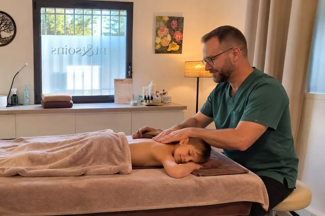 Bernard Carret-Ollivier masse le dos d’un enfant allongé sur la table de massage du cabinet, le visage posé dans l’appui-tête.